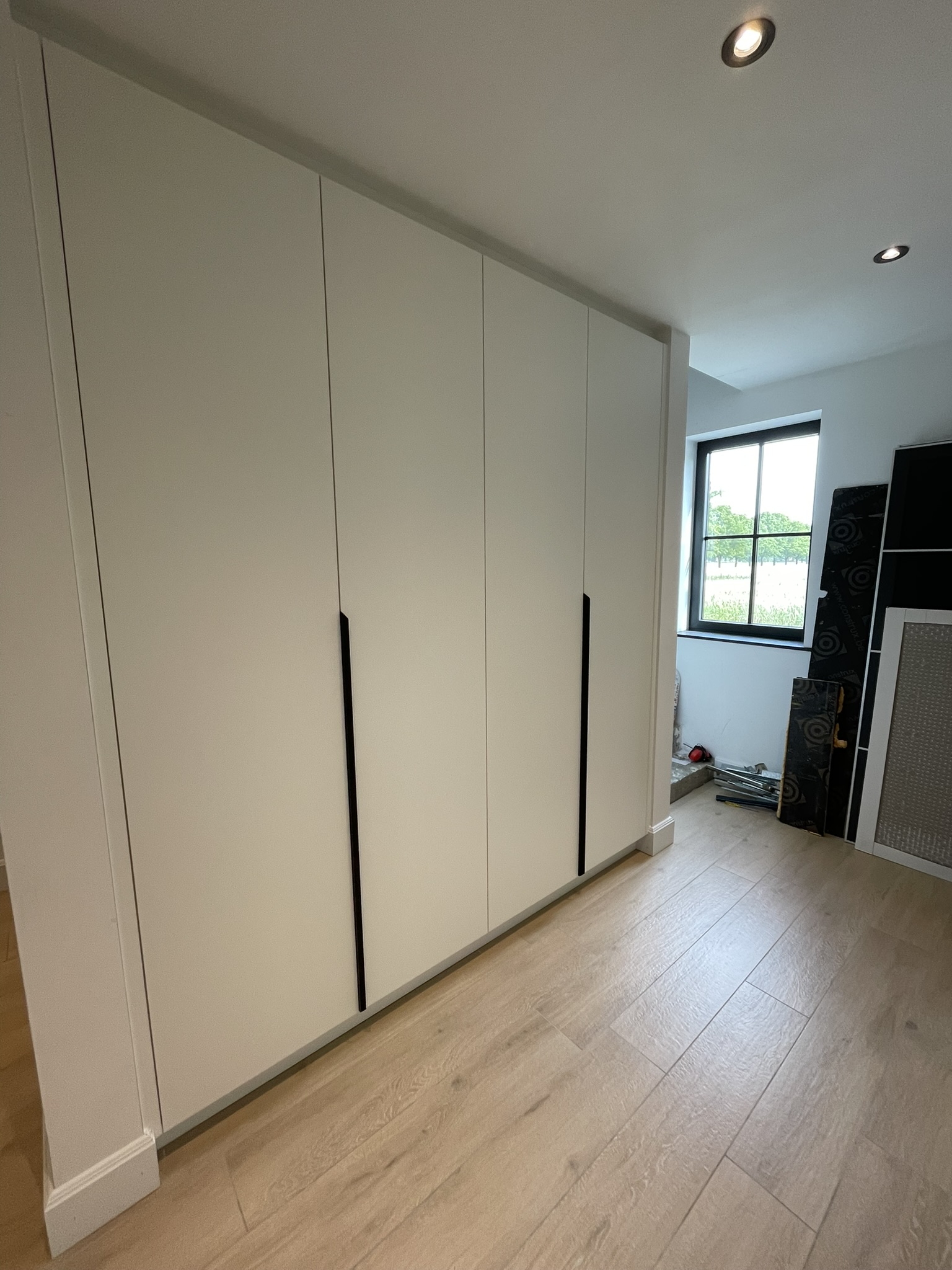 Witte kastenwand in de gang met vlakke fronten en lange zwarte grepen